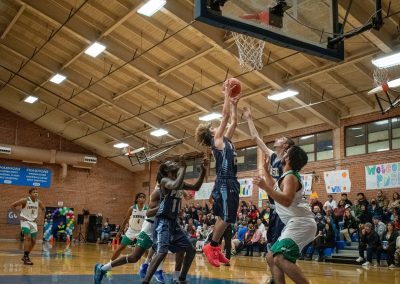A photograph of an active WSBC basketball game in the ASDB gymnasium. On court are the competing Phoenix Roadrunner and Washington Terrier boys teams. In the photo, a Roadrunner player prepares to collect a rebound with both hands.