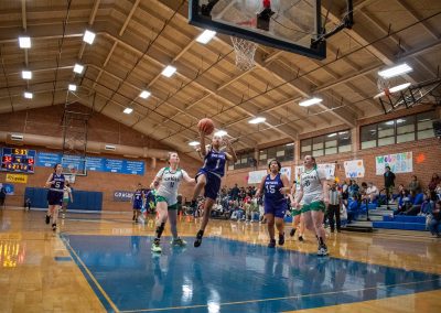 A photograph of an active WSBC basketball game in the ASDB gymnasium. On court are the competing Oregon Panther and Washington Terrier girls teams. In the photo, a lone Panther player is attempting an unguarded layup.
