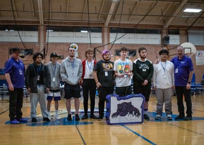 A photo of the entire Oregon Panther boys team in the ASDB gymnasium. They are standing shoulder-to-shoulder with large smiles on their faces. On the ground in front of them is a purple and white piñata printed with their team logo.