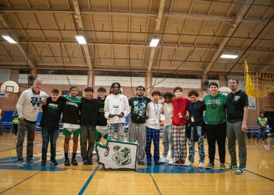A photo of the entire Washington Terrier boys team in the ASDB gymnasium. They are standing with their arms wrapped around one another, and large smiles on their faces. On the ground in front of them is a green and white piñata printed with their team logo.
