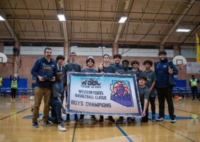 A photo of the entire Phoenix Roadrunner boys team in the ASDB gymnasium. They are posing together with large smiles on their faces. They are collectively holding up a large banner reading, 'WSBC Tucson, AZ 2024 Western States Basketball Classic Boys Champions'.