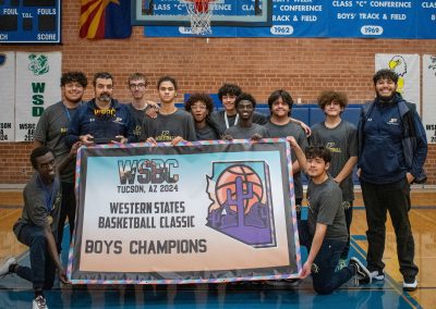 A photo of the entire Phoenix Roadrunner boys team in the ASDB gymnasium. They are posing together with large smiles on their faces. Two players hold up a large banner reading, 'WSBC Tucson, AZ 2024 Western States Basketball Classic Boys Champions'.