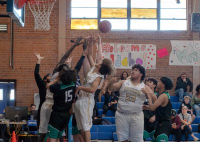A photograph of an active WSBC basketball game in the ASDB gymnasium. On court are the competing Washington Terrier and Phoenix Roadrunner boys teams. In the photo, a crowd of players from both teams attempts to secure a rebounding basketball.