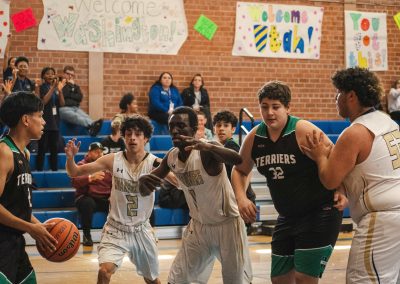 A photograph of an active WSBC basketball game in the ASDB gymnasium. On court are the competing Washington Terrier and Phoenix Roadrunner boys teams. In the photo, a Terrier player looks to pass between three defenders towards an open teammate.