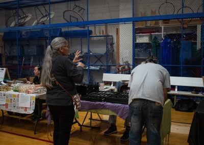 A photo of a temporary table set-up in the ASDB gymnasium. Placed on top of the table are open cases filled with decorative jewelry. Two individuals look over the jewelry with their backs to the camera.