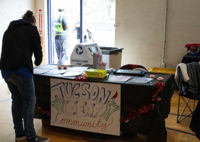 A photo of a temporary table set up in the ASDB gymnasium lobby. The table is draped in a large, black tablecloth with an attached poster reading, 'Tucson Deaf Community.' An individual stands just to the left of the table and studies a piece of paper.