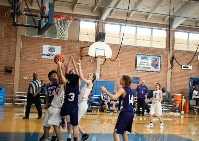 A photograph of an active WSBC basketball game in the ASDB gymnasium. On court are the competing Oregon Panther and Idaho Raptor boys teams. In the photo, a Raptor player attempts to score amidst a crowd of players from both teams.