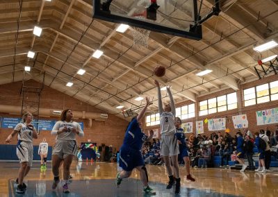 A photograph of an active WSBC basketball game in the ASDB gymnasium. On court are the competing Utah Eagle and Arizona Sentinel girls teams. In the photo, a Sentinel player attempts a two-point shot over the hands of an Eagle defender.