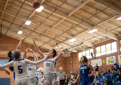 A photograph of an active WSBC basketball game in the ASDB gymnasium. On court are the competing Utah Eagle and Arizona Sentinel girls teams. In the photo, a Sentinel player releases her shot attempt over the hand of an Eagle defender.