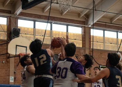 A photograph of an active WSBC basketball game in the ASDB gymnasium. On court are the competing Phoenix Roadrunner and Oregon Panther boys teams. In the close-up photo, a crowd of players from both teams end up blocking an Oregon player's shot attempt.