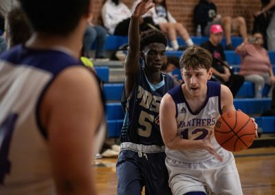 A photograph of an active WSBC basketball game in the ASDB gymnasium. On court are the competing Phoenix Roadrunner and Oregon Panther boys teams. In the close-up photo, a determined Panther player looks for an offensive opening while being guarded by a defender.