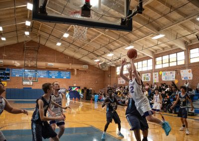 A photograph of an active WSBC basketball game in the ASDB gymnasium. On court are the competing Phoenix Roadrunner and Oregon Panther boys teams. In the photo, a Panther player attempts a leaping layup from beyond the paint.