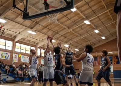 A photograph of an active WSBC basketball game in the ASDB gymnasium. On court are the competing Phoenix Roadrunner and Oregon Panther boys teams. In the photo, a Panther players prepares to shoot a two-pointer over two Roadrunner defenders.