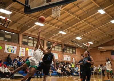 A photograph of an active WSBC basketball game in the ASDB gymnasium. On court are the competing Arizona Sentinel and Washington Terrier boys teams. In the photo, a Terrier player is pictured falling just as he attempts a layup.