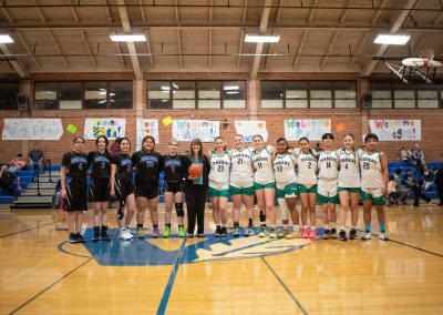 A photo of both the Washington Terrier and Arizona Sentinel girls teams gathered in the ASDB gymnasium. They are posing together with large smiles on their faces. Standing in between both teams, with a large smile on her face, is ASDB Superintendent Annette Reichman.