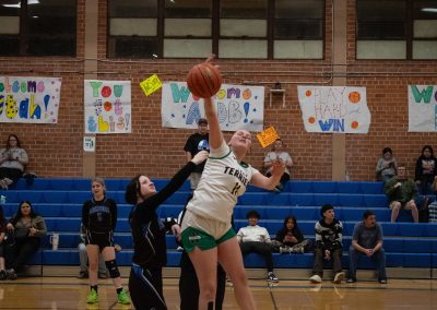 A photo of ASDB Superintendent Annette Reichman leading the basketball tip off. She is flanked on either side by a respective player from the Arizona Sentinel and Washington Terrier girls teams. In the photo, the Terrier player leaps above the Sentinel player and smacks the basketball back towards her team.