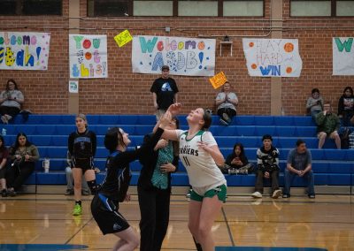 A photo of ASDB Superintendent Annette Reichman leading the basketball tip off. She is flanked on either side by a respective player from the Arizona Sentinel and Washington Terrier girls teams. Each player looks up at the basketball as it is tossed in the air.