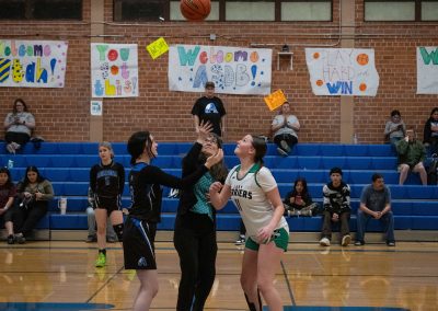 A photo of ASDB Superintendent Annette Reichman leading the basketball tip off. She is flanked on either side by a respective player from the Arizona Sentinel and Washington Terrier girls teams. Each player looks up at the basketball as it is tossed in the air.