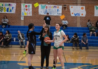 A photo of ASDB Superintendent Annette Reichman preparing to lead the basketball tip off. She is flanked on either side by a respective player from the Arizona Sentinel and Washington Terrier girls teams.