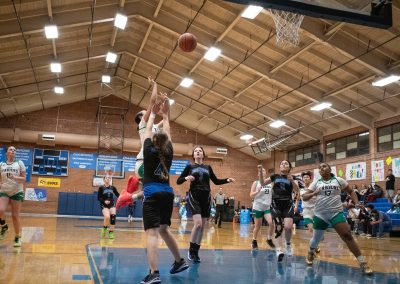 A photograph of an active WSBC basketball game in the ASDB gymnasium. On court are the competing Arizona Sentinel and Washington Terrier girls teams. In the photo, a Terrier player attempts to recover an offensive rebound before a Sentinel defender.