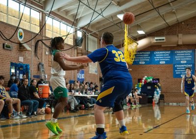 A photograph of an active WSBC basketball game in the ASDB gymnasium. On court are the competing Utah Eagles and Washington Terrier boys teams. In the photo, a Terrier player prepares to receive a lob pass from a teammate.