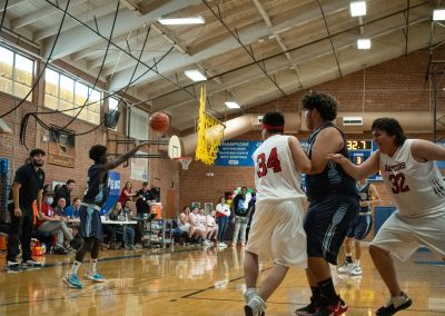 A photograph of an active WSBC basketball game in the ASDB gymnasium. On court are the competing Phoenix Roadrunner and Idaho Raptor boys teams. In the photo, a Roadrunner player is passing the basketball towards a teammate at the top of the arc.