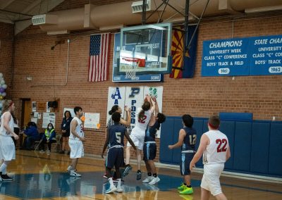 A photograph of an active WSBC basketball game in the ASDB gymnasium. On court are the competing Phoenix Roadrunner and Idaho Raptor boys teams. In the photo, a Roadrunner and Raptor player wrestle for a basketball rebound.
