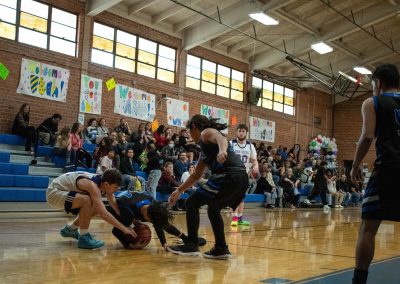 A photograph of an active WSBC basketball game in the ASDB gymnasium. On court are the competing Arizona Sentinel and Oregon Panther boys teams. In the photo, a Sentinel player falls on the basketball just as an Oregon defender attempts to swipe it.