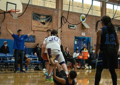 A photograph of an active WSBC basketball game in the ASDB gymnasium. On court are the competing Arizona Sentinel and Oregon Panther boys teams. In the photo, a Panther player is snatching the basketball from a fallen Sentinel player.