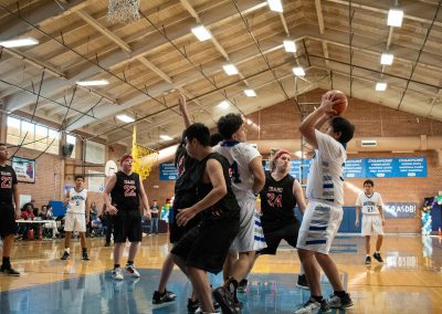 A photograph of an active WSBC basketball game in the ASDB gymnasium. On court are the competing Idaho Raptor and Arizona Sentinel boys teams. In the photo, a Sentinel player sets an offensive screen so the teammate behind him can attempt a shot.