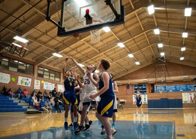 A photograph of an active WSBC basketball game in the ASDB gymnasium. On court are the competing Utah Eagle and Oregon Panther boys teams. In the photo, an Eagle player attempts a shooting layup over the arm of a Panther defender.