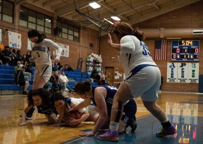 A photograph of an active WSBC basketball game in the ASDB gymnasium. On court are the competing Oregon Panther and Arizona Sentinel girls teams. In the photo, players from both teams are pictured falling on a loose basketball.