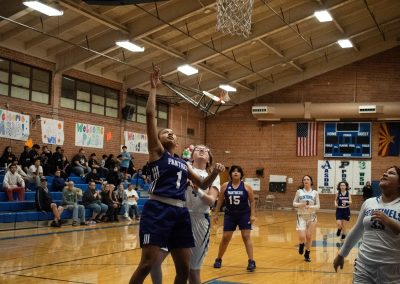 A photograph of an active WSBC basketball game in the ASDB gymnasium. On court are the competing Oregon Panther and Arizona Sentinel girls teams. In the photo, a Panther player eagerly waits to see if her attempted layup will score two points.