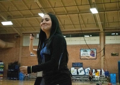 A photograph of a student in the ASDB gymnasium. She has long black hair and wears a jet black jersey which reads, 'Arizona, 11.' She is pictured smiling sheepishly.