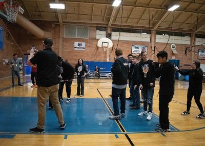 A photograph of an individual striking a piñata in the ASDB gymnasium. The piñata is intended for the Idaho Raptor basketball team. Behind the piñata is the rest of the Raptor basketball team waiting for their turn to swing.
