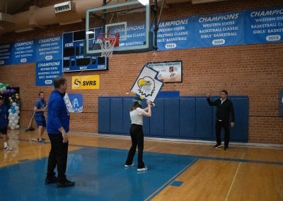 A photograph of a blindfolded student striking a piñata in the ASDB gymnasium. The piñata is colored blue and white, and is printed with the Utah Eagle's athletic logo. It is also crafted to look like the state of Utah.