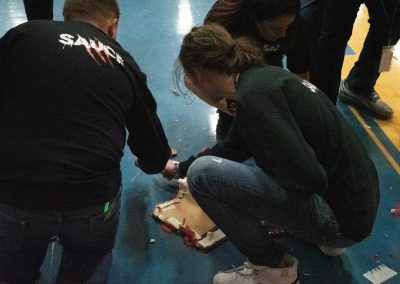 An over-the-shoulder photograph of the ASDB gymnasium floor. Spread across the floor are remnants of a red and white piñata, as well as various bits of candy. A handful of students are pictured collecting the candy.