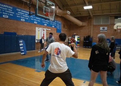 A photograph of an individual striking a piñata in the ASDB gymnasium. The piñata is colored blue and white, and is crafted to look like the state of Arizona. Behind them is a line of students waiting for their turn to swing at the decoration.